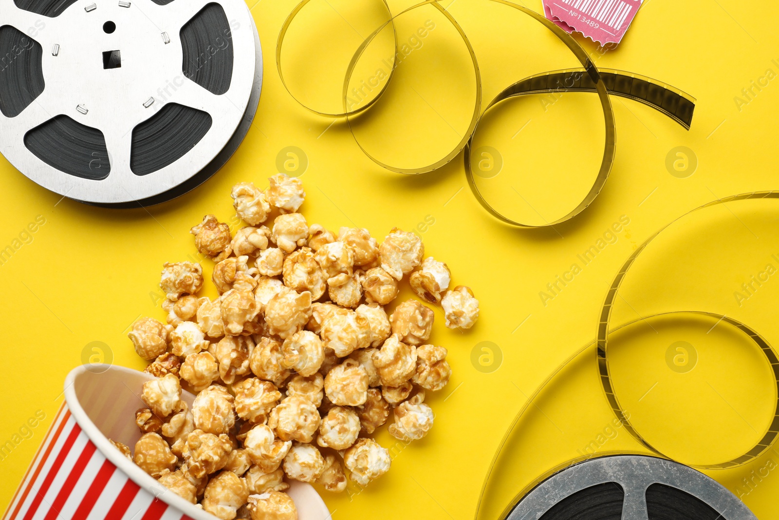 Photo of Sweet popcorn and film reels on yellow background, flat lay