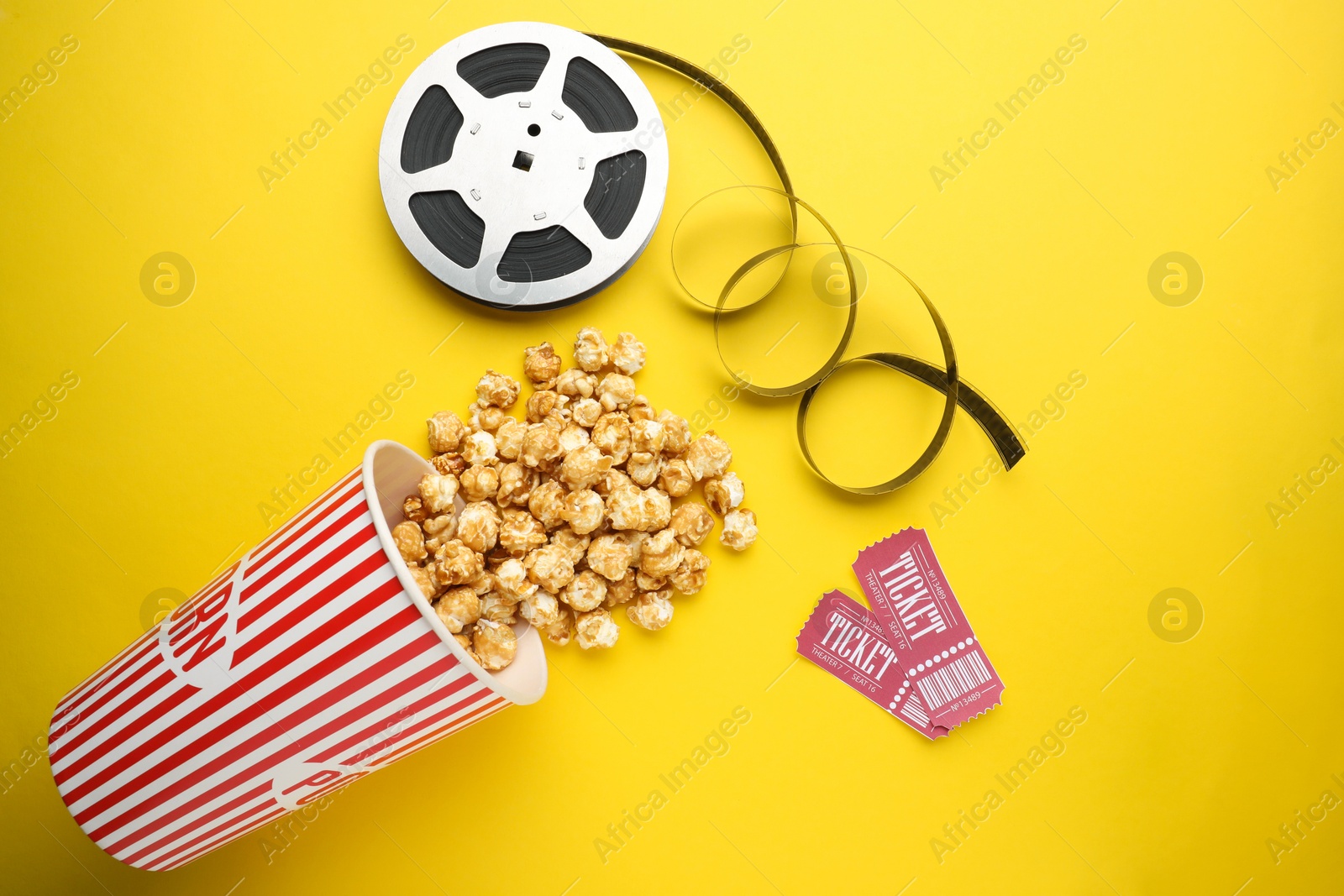 Photo of Movie tickets, sweet popcorn and film reel on yellow background, flat lay