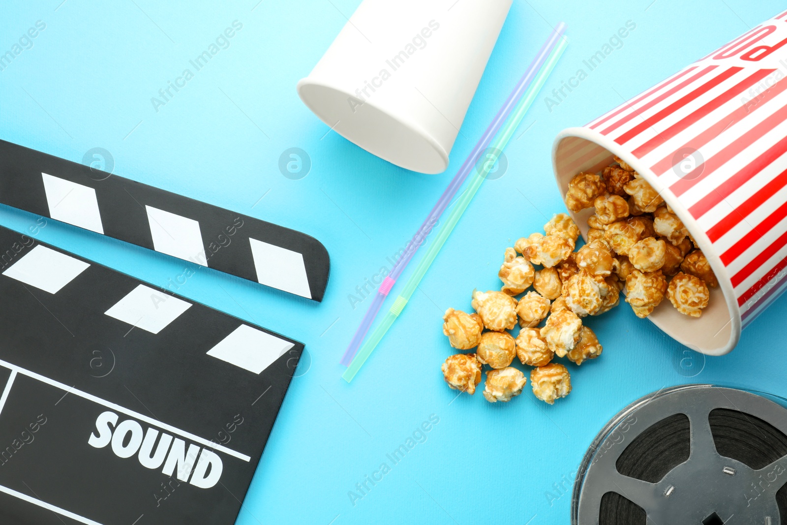 Photo of Movie clapper, sweet popcorn and film reel on light blue background, flat lay