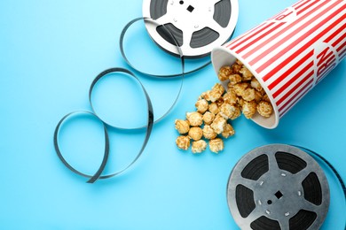 Photo of Sweet popcorn and film reels on light blue background, flat lay