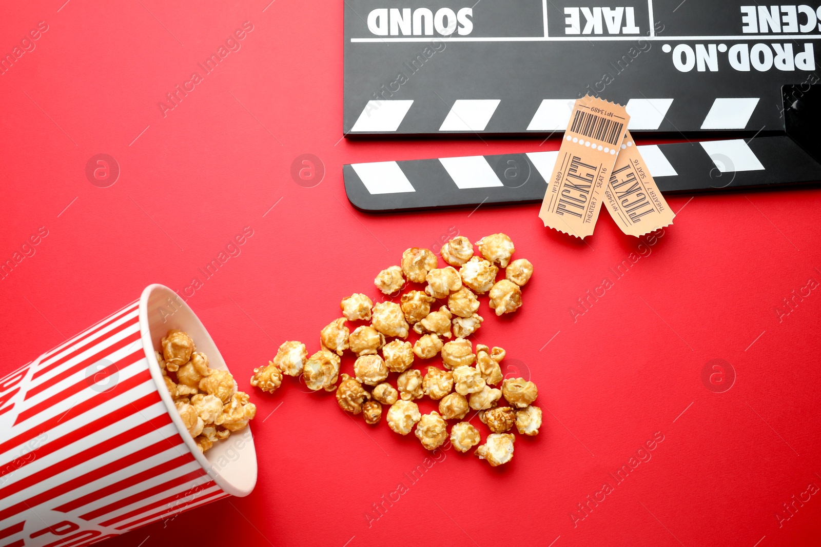 Photo of Movie clapper, sweet popcorn and tickets on red background, flat lay