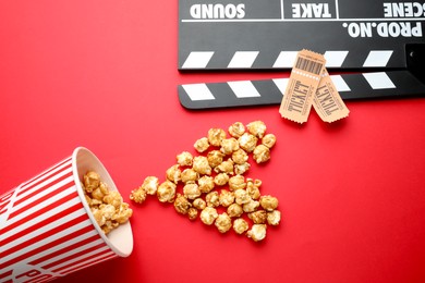 Photo of Movie clapper, sweet popcorn and tickets on red background, flat lay