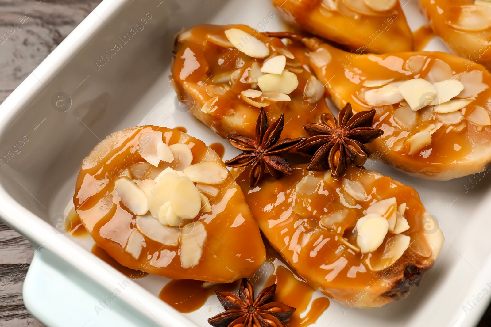 Photo of Delicious pears with caramel sauce, almond flakes and anise stars in baking dish on table, closeup