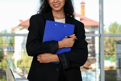 Photo of Young woman with clipboard wearing stylish suit indoors, closeup