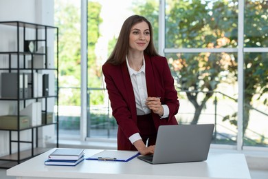 Photo of Portrait of young woman with laptop wearing stylish suit at white table indoors