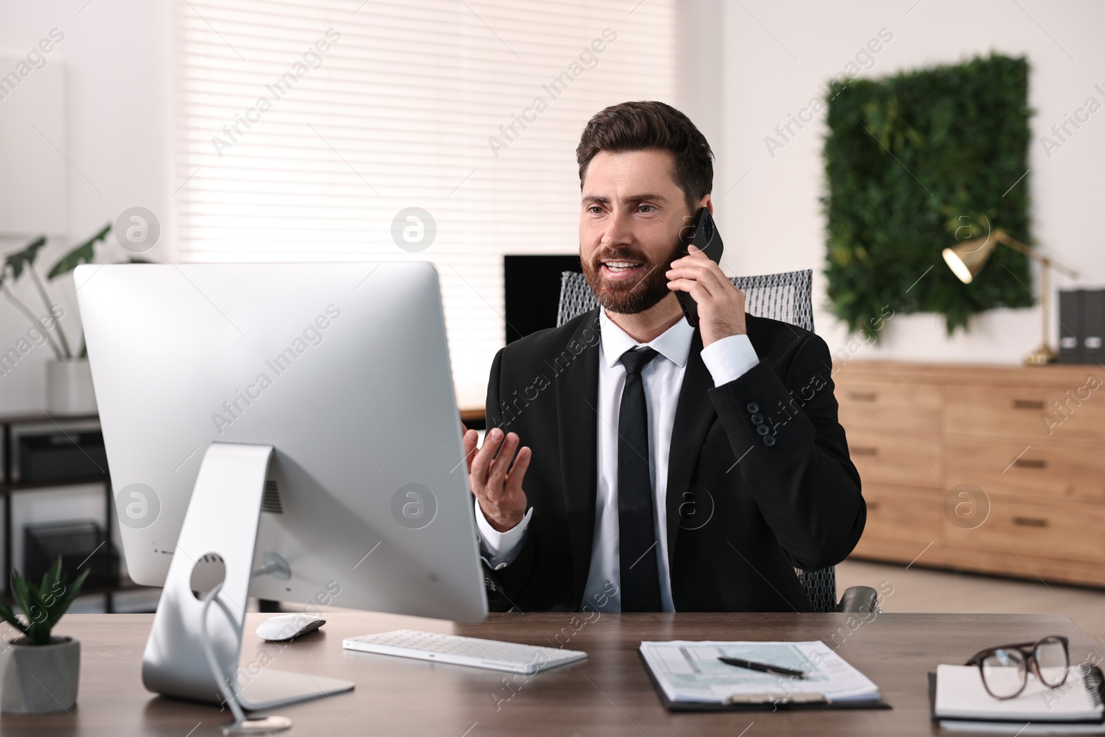 Photo of Man talking on smartphone while working at table in office