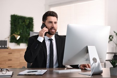 Photo of Man talking on smartphone while working at table in office