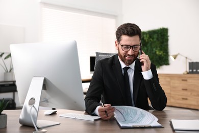 Photo of Man talking on smartphone while working at table in office