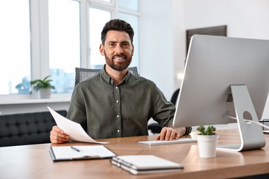 Photo of Man with document working on computer at table in office