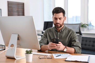 Photo of Man using smartphone at table in office