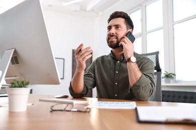 Photo of Man talking on smartphone while working at table in office