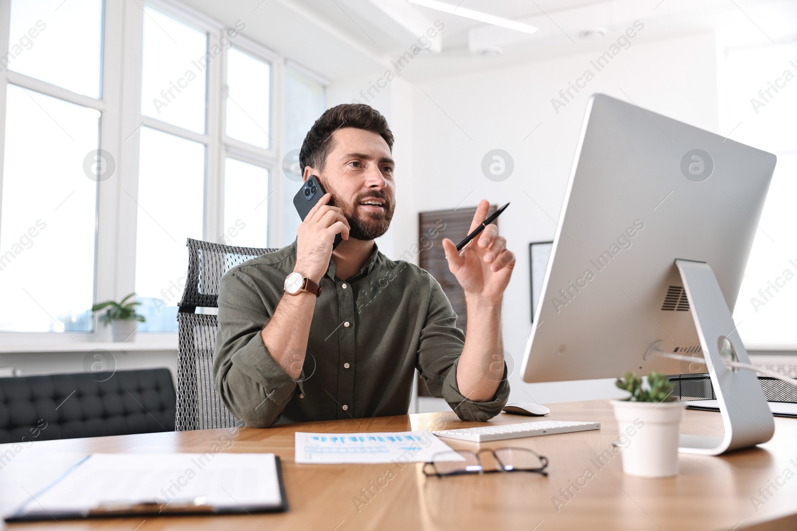 Photo of Man talking on smartphone while working at table in office