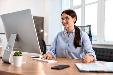 Photo of Woman taking notes while working on computer at table in office