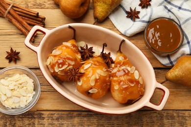 Photo of Delicious pears with caramel sauce, almond flakes and spices on wooden table, top view