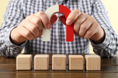 Photo of Man with magnet attracting cubes at wooden table, closeup