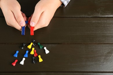 Photo of Man with magnet attracting game pieces at wooden table, above view. Space for text