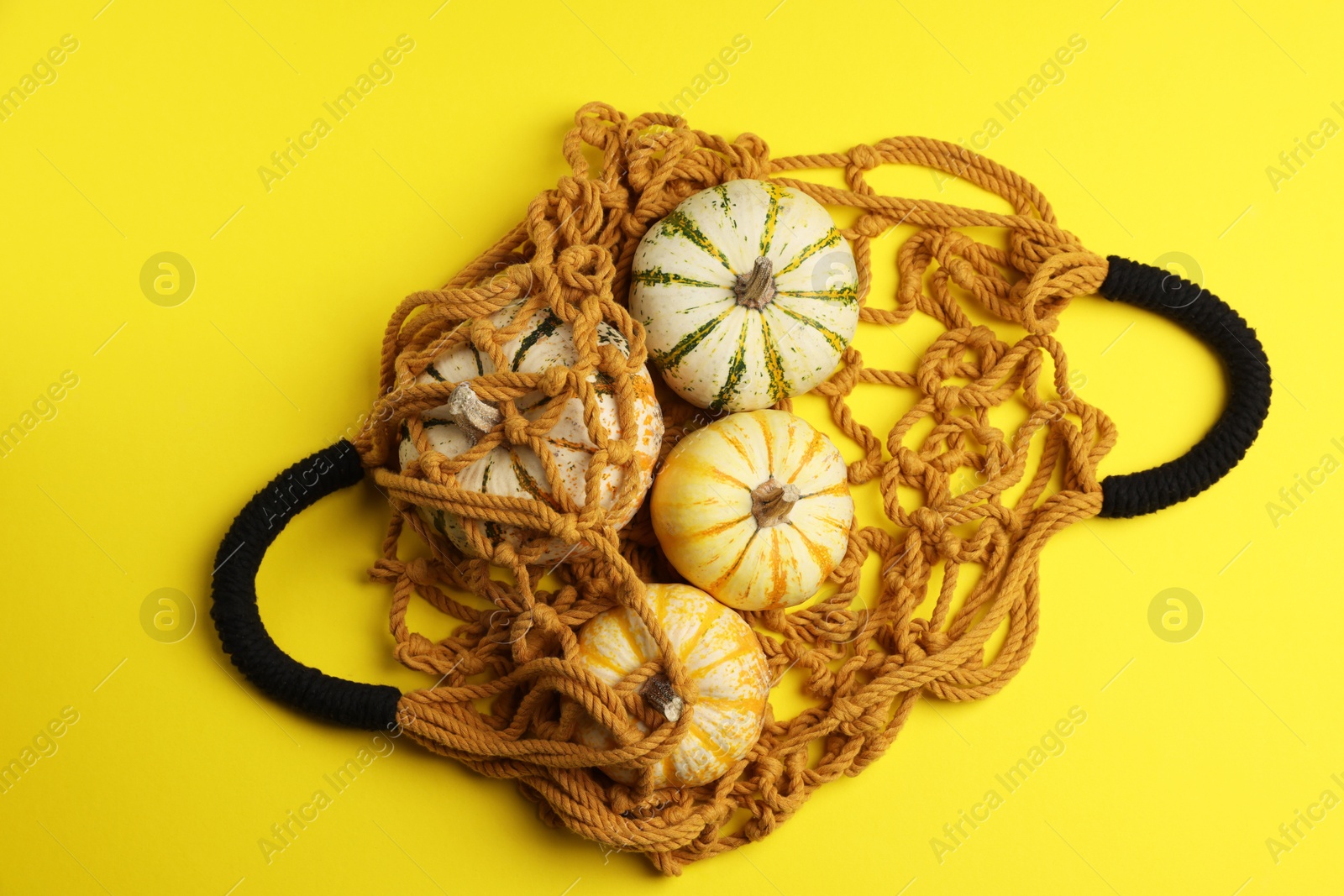 Photo of Macrame shopping bag and pumpkins on yellow background, top view