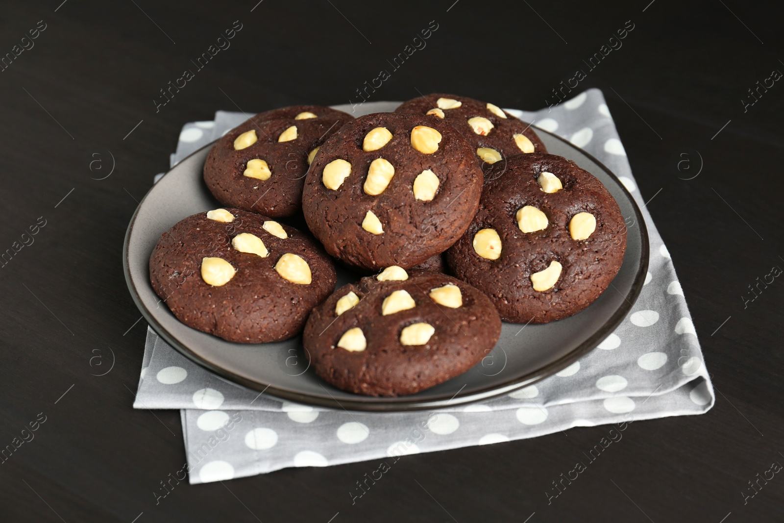 Photo of Delicious chocolate cookies with hazelnuts on black wooden table