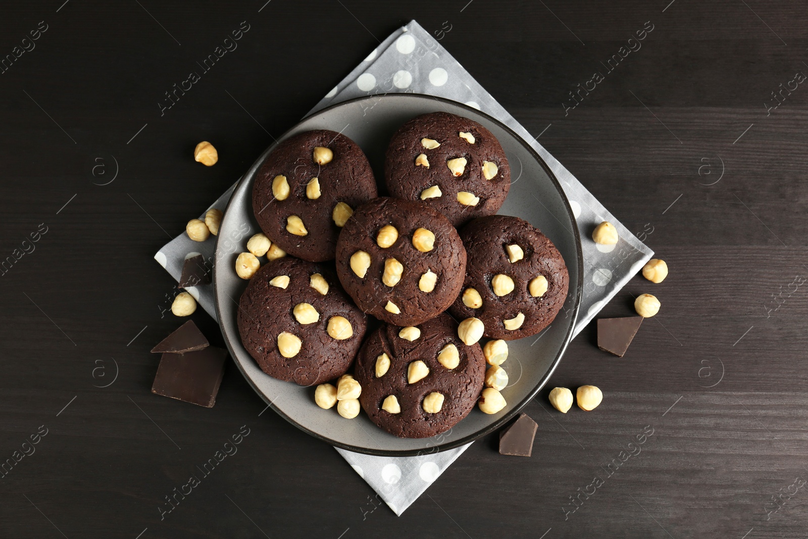 Photo of Delicious chocolate cookies with hazelnuts on black wooden table, flat lay