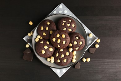 Photo of Delicious chocolate cookies with hazelnuts on black wooden table, flat lay