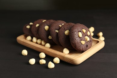 Photo of Delicious chocolate cookies with hazelnuts on black wooden table, closeup