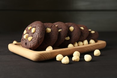 Photo of Delicious chocolate cookies with hazelnuts on black wooden table, closeup