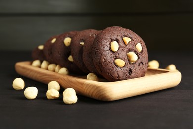 Photo of Delicious chocolate cookies with hazelnuts on black wooden table, closeup