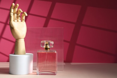 Photo of Bottle of fragrant perfume and wooden mannequin hand on white table against pink background, space for text