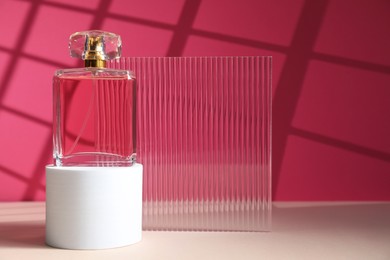 Photo of Stylish presentation of perfume bottle on white table against pink background, space for text