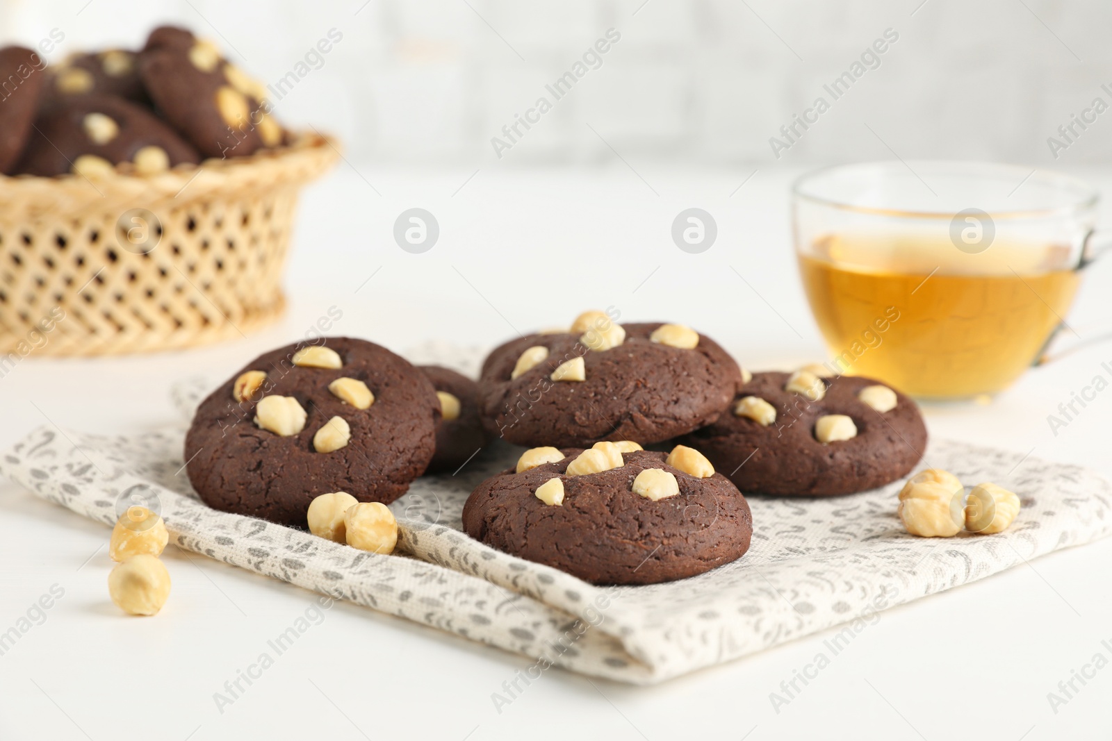 Photo of Tasty chocolate cookies with hazelnuts and tea on white table, closeup