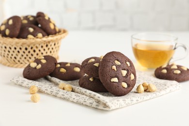 Photo of Tasty chocolate cookies with hazelnuts and tea on white table, closeup