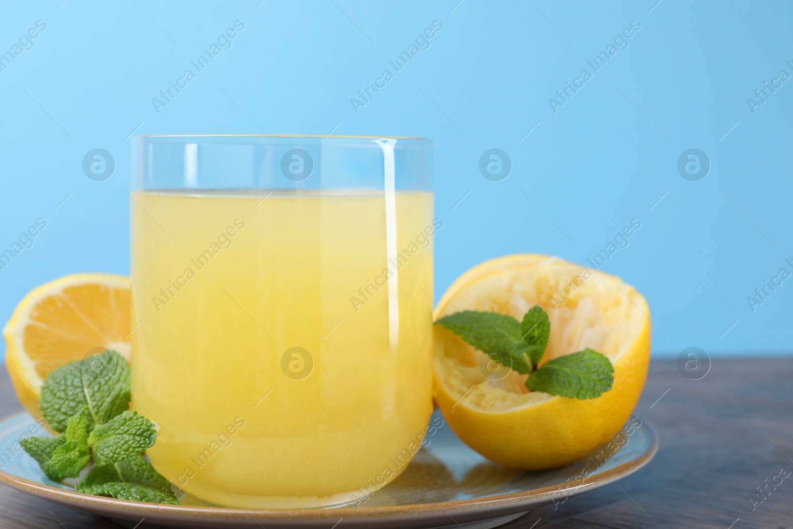 Photo of Glass of lemon juice and fresh fruits on wooden table, closeup