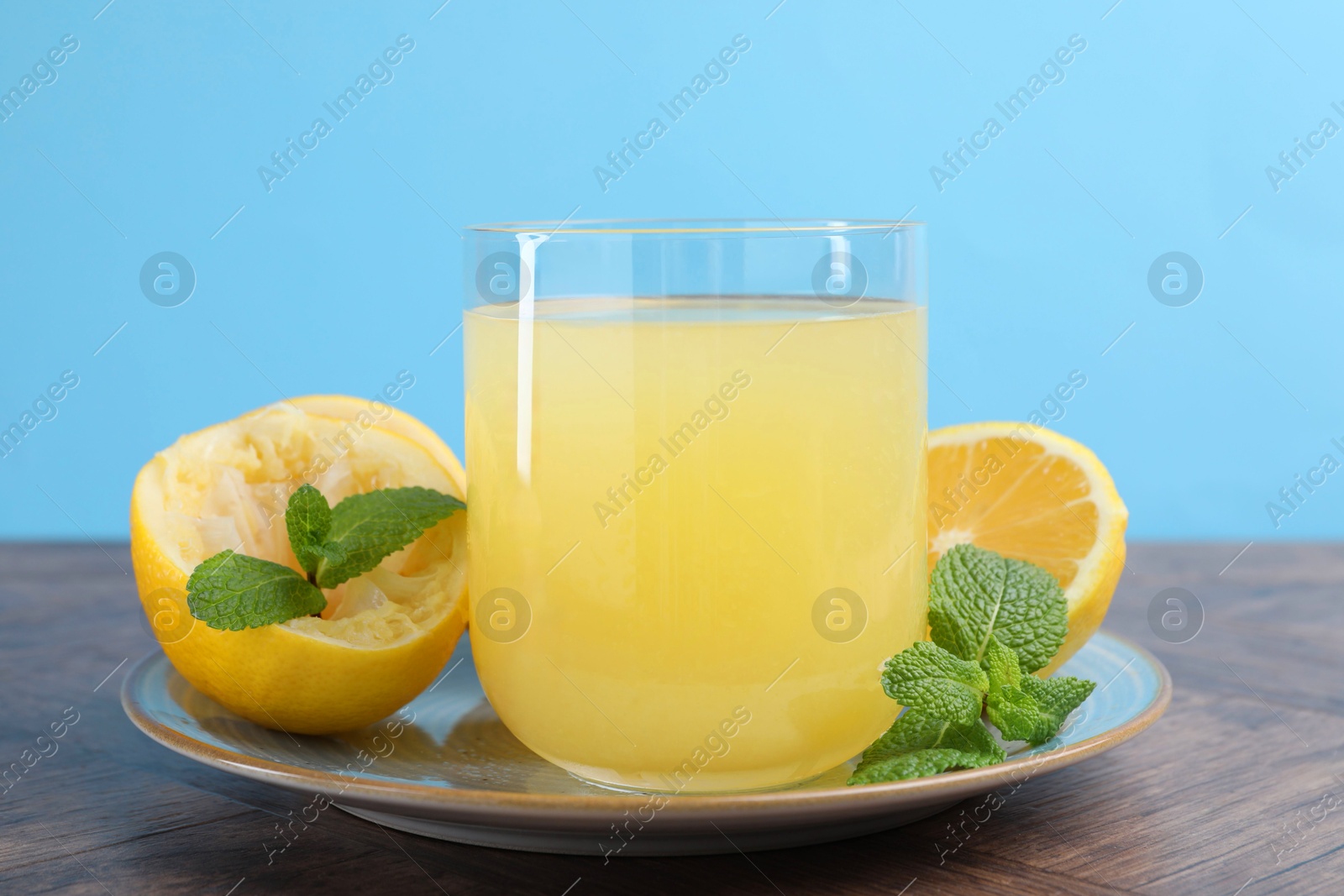 Photo of Glass of lemon juice and fresh fruits on wooden table, closeup