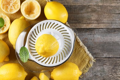 Photo of Juicer and fresh lemons on wooden table, top view. Space for text