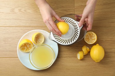 Photo of Woman with lemon using juicer at wooden table, top view