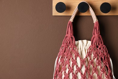 Photo of Handmade macrame shopping bag on brown wall, space for text