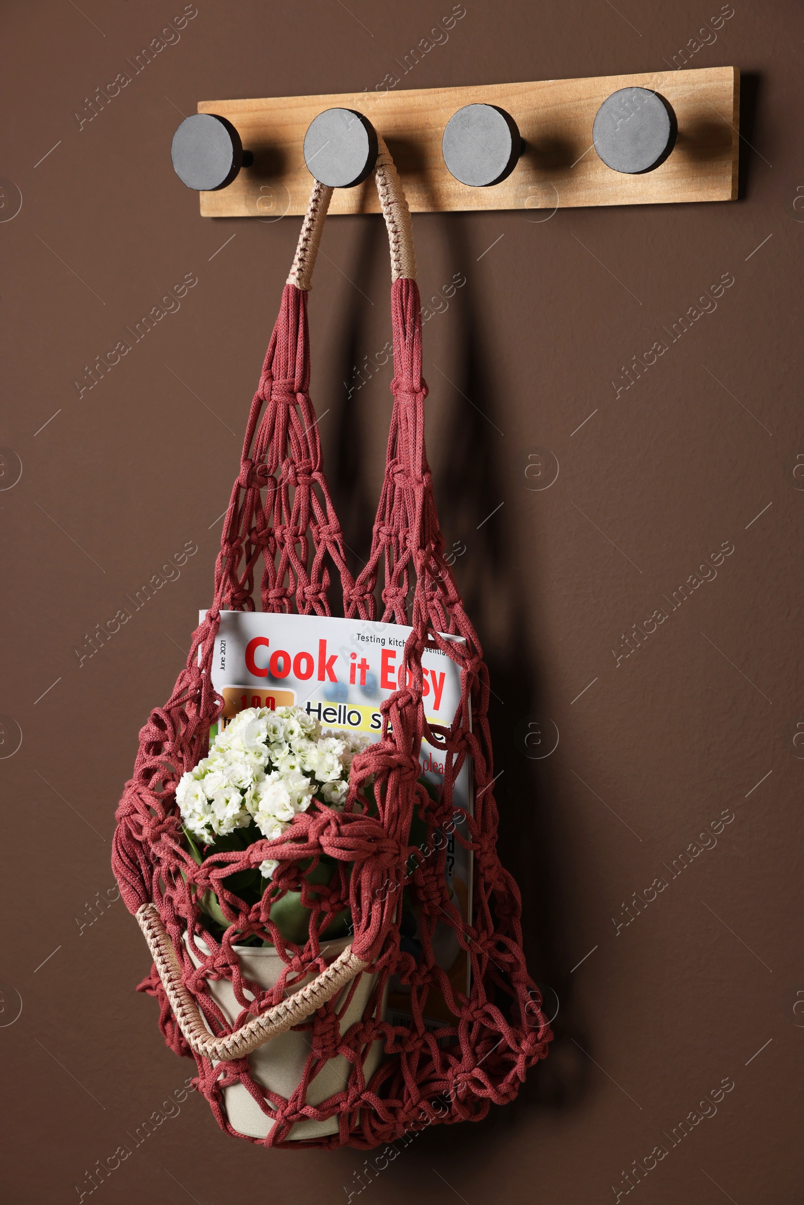 Photo of Handmade macrame shopping bag with magazine and flowers on brown wall