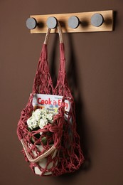 Photo of Handmade macrame shopping bag with magazine and flowers on brown wall