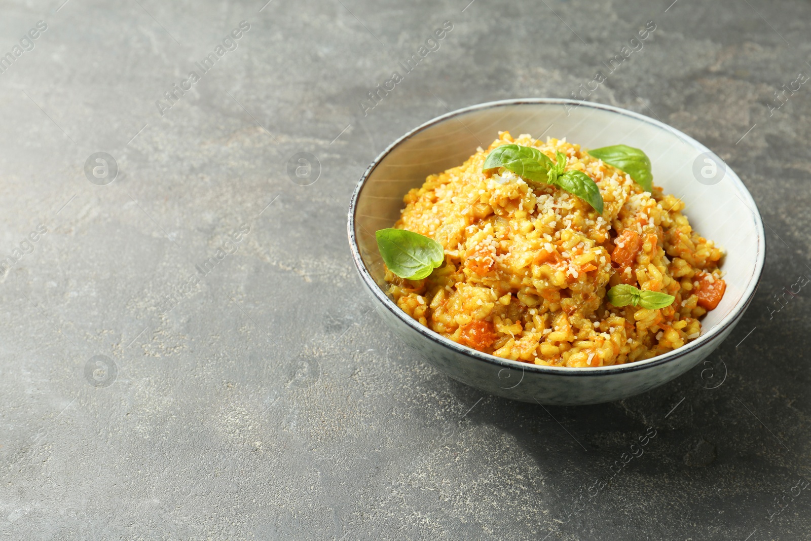 Photo of Delicious pumpkin risotto with basil on grey table. Space for text
