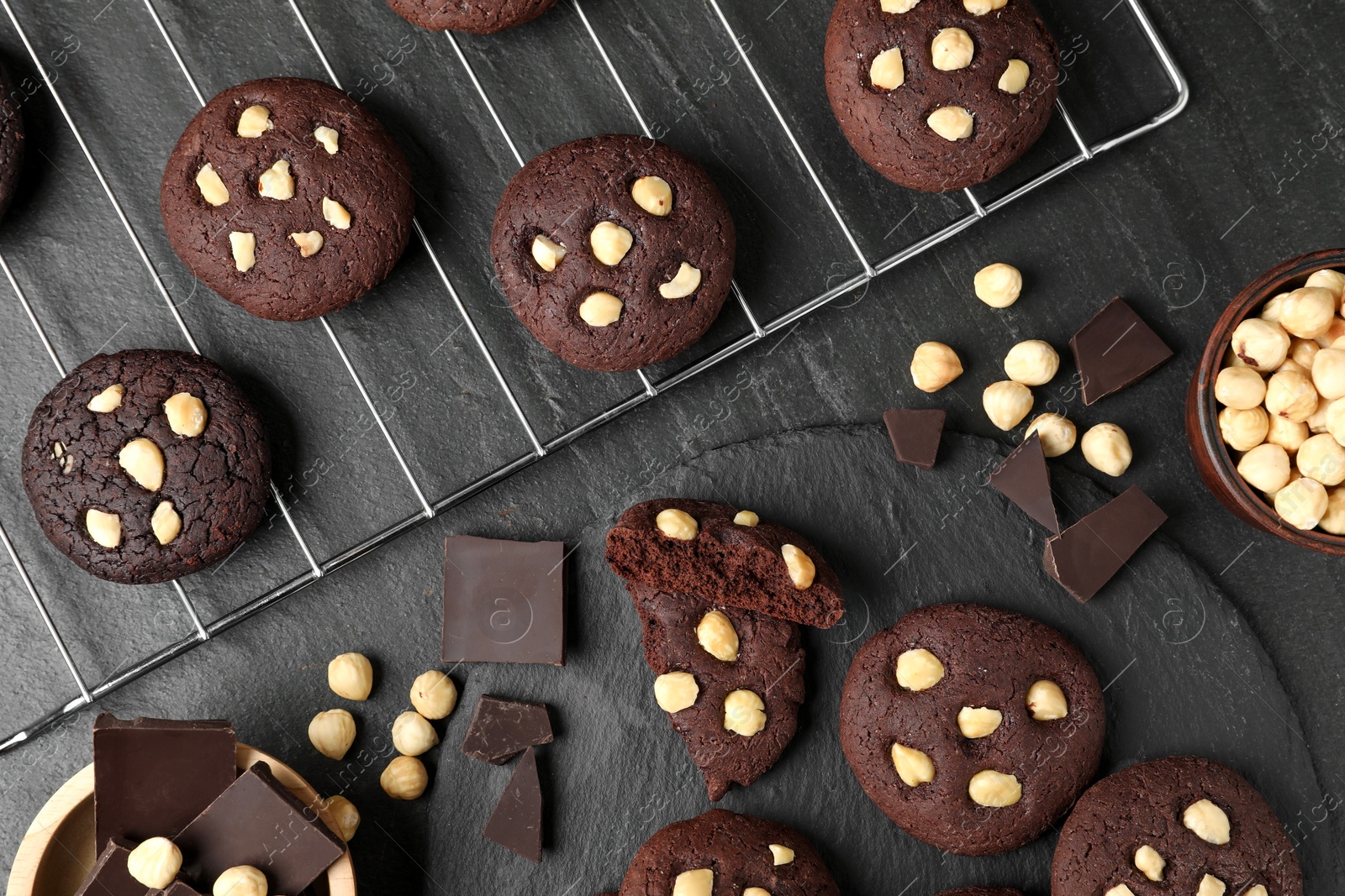 Photo of Tasty chocolate cookies with hazelnuts on black table, flat lay