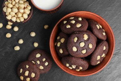 Photo of Tasty chocolate cookies with hazelnuts and milk on black table, flat lay