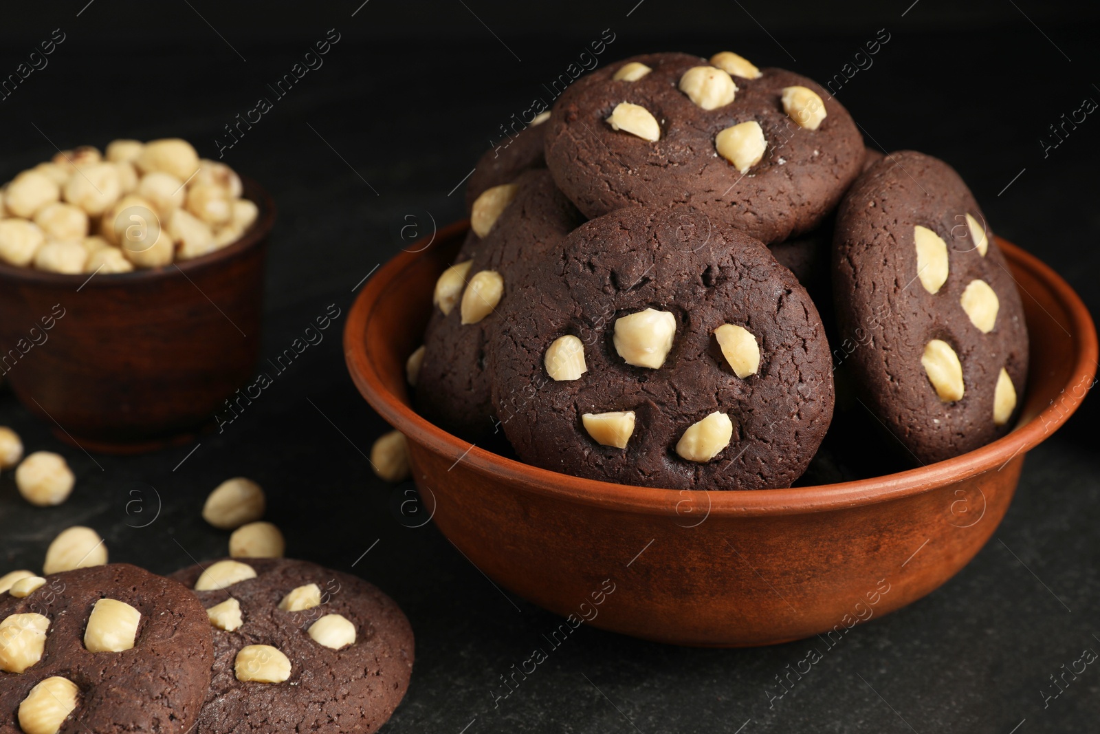 Photo of Tasty chocolate cookies with hazelnuts on black table, closeup