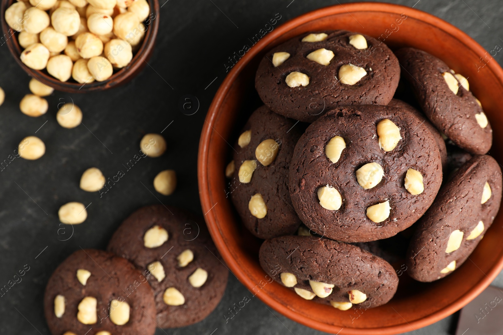 Photo of Tasty chocolate cookies with hazelnuts on black table, flat lay