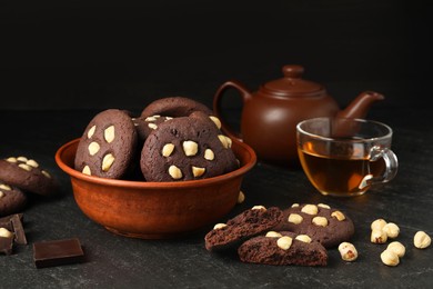 Photo of Tasty chocolate cookies with hazelnuts and tea on black table