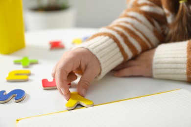 Photo of Little girl learning alphabet with magnetic letters at white table, closeup