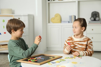 Photo of Little kids learning alphabet with magnetic letters at white table indoors