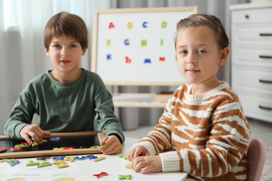 Photo of Little kids learning alphabet with magnetic letters at white table indoors