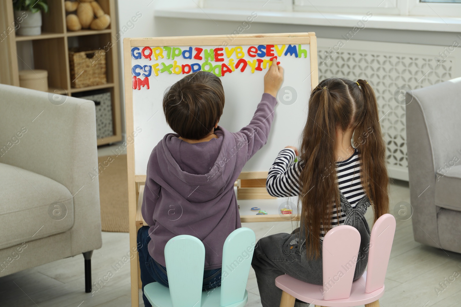 Photo of Little kids learning alphabet with magnetic letters indoors, back view