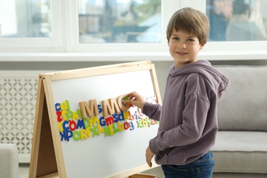 Photo of Little boy learning alphabet with different letters on board indoors