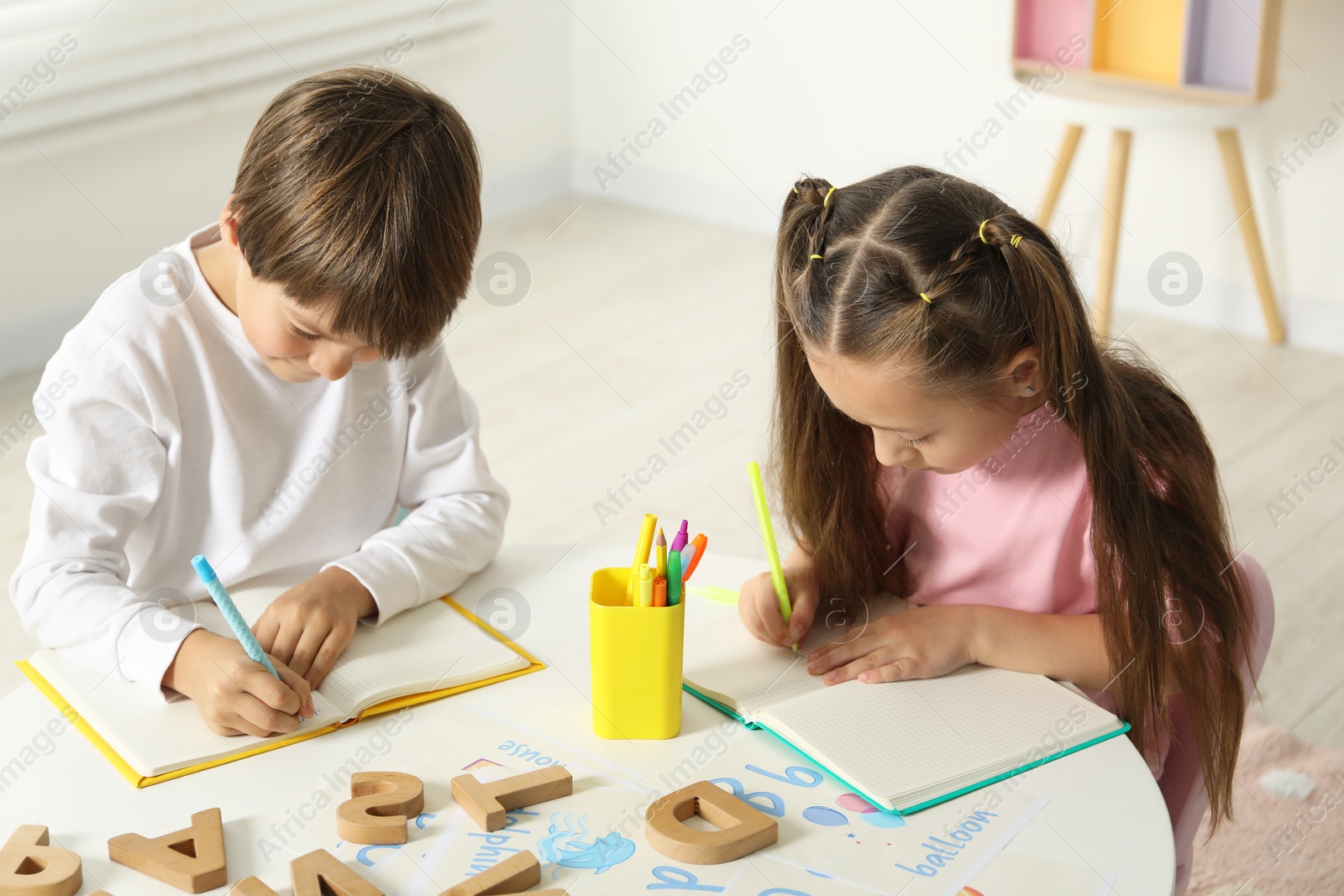 Photo of Little kids learning alphabet at white table indoors